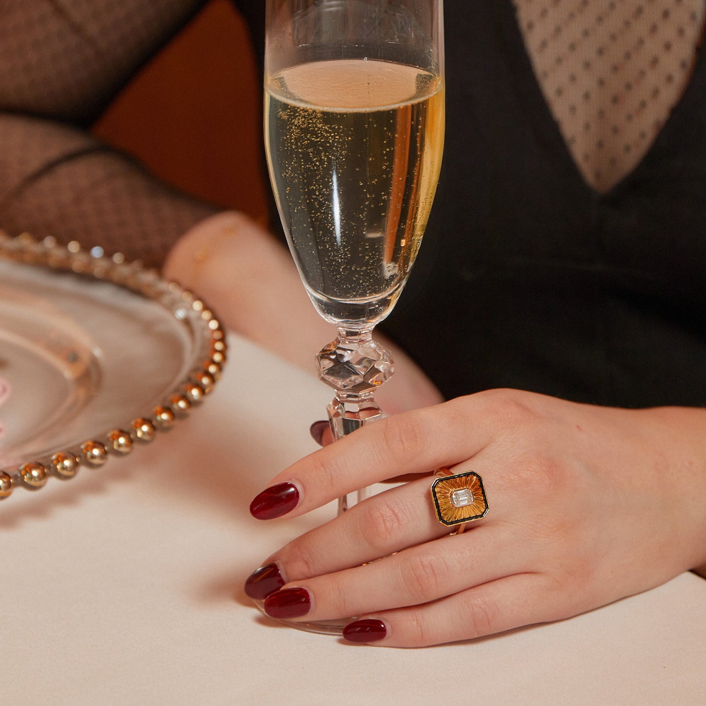 Hand model holding champagne and wearing New York Collection Art Deco Diamond Gold Cocktail Ring with a 0.5ct octagon cut diamond and black enamel from Augustine Jewels